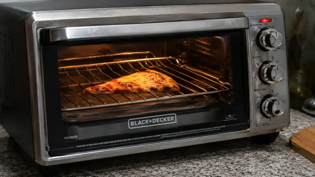 Hand placing a small baking pan with roasted vegetables into the BLACK+DECKER TO1760SS toaster oven